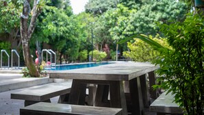A concrete poolside area with picnic tables and a pool in the background. - Muntra Garden Resort (Sattahip)