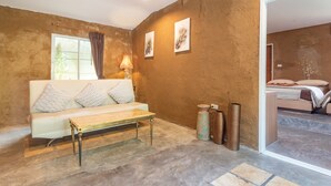A room with a white sofa, a wooden coffee table, and a large window with curtains. There are two wall-mounted lamps and two framed artworks. - Muntra Garden Resort (Sattahip)