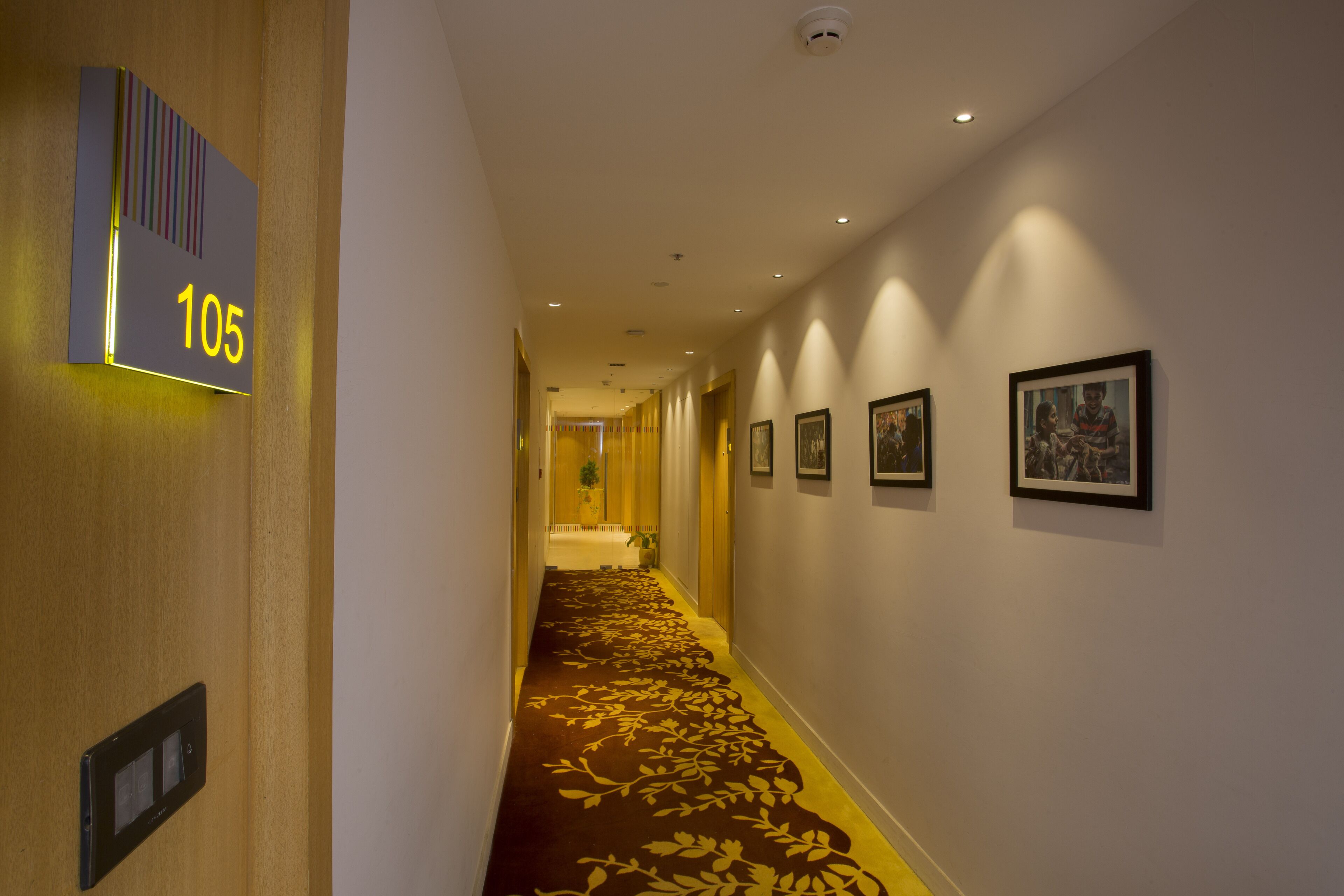 A hotel hallway with a carpeted floor, a number sign, and framed pictures on the wall.