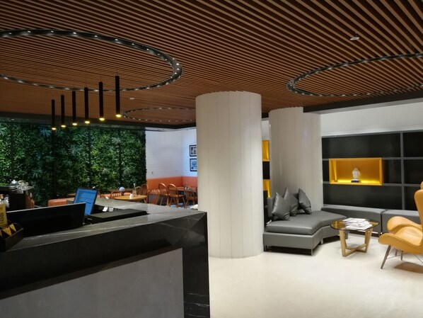 Un interior moderno con una recepción, una zona de estar y una pared verde.