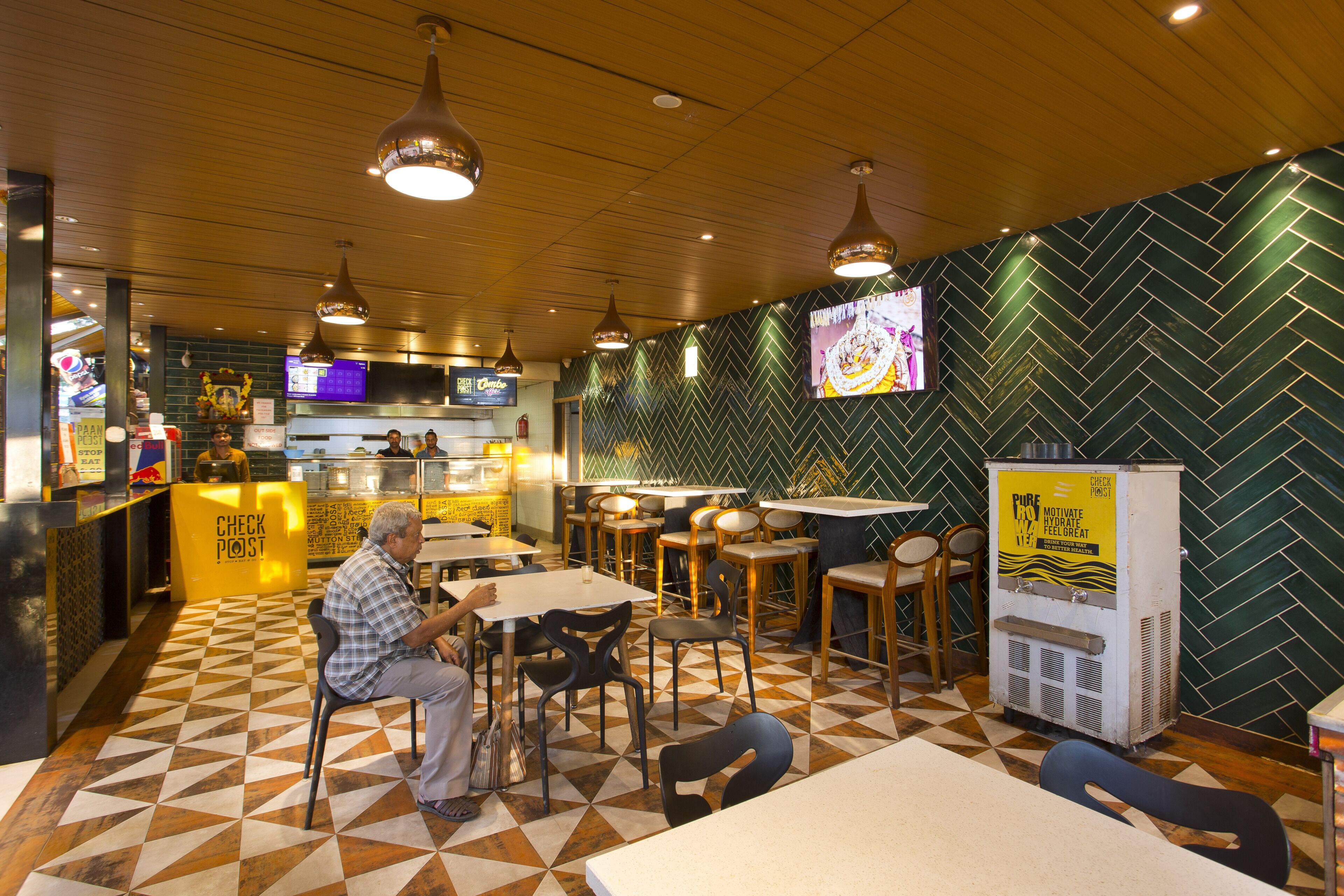 Interior de un restaurante con mostradores de recepción, zonas de estar y dispensador de bebidas.