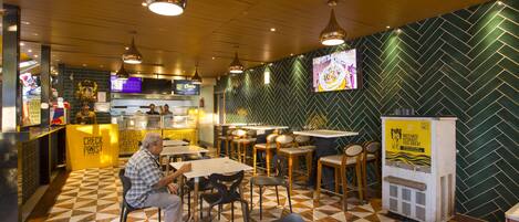 Interior de un restaurante con mostradores de recepción, zonas de estar y dispensador de bebidas.