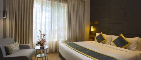 A hotel room with a large bed, a sofa, a small table with a vase of flowers, and a large window with curtains.