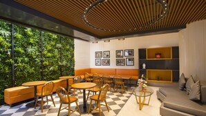 A modern lounge area with wooden furniture, a checkered floor, and a green wall with plants. - Fountain Tree by TGI (Bengaluru)