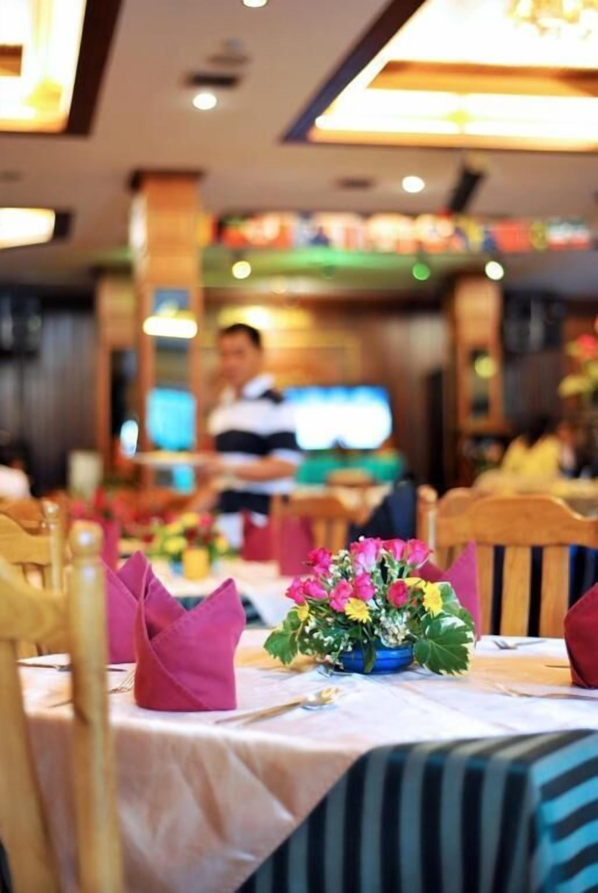 Interior de restaurante con mesas dispuestas para comer, un camarero al fondo y un centro de mesa floral.