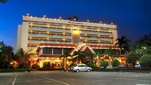 Un hotel de varios pisos con una entrada destacada y un estacionamiento frente a él.
