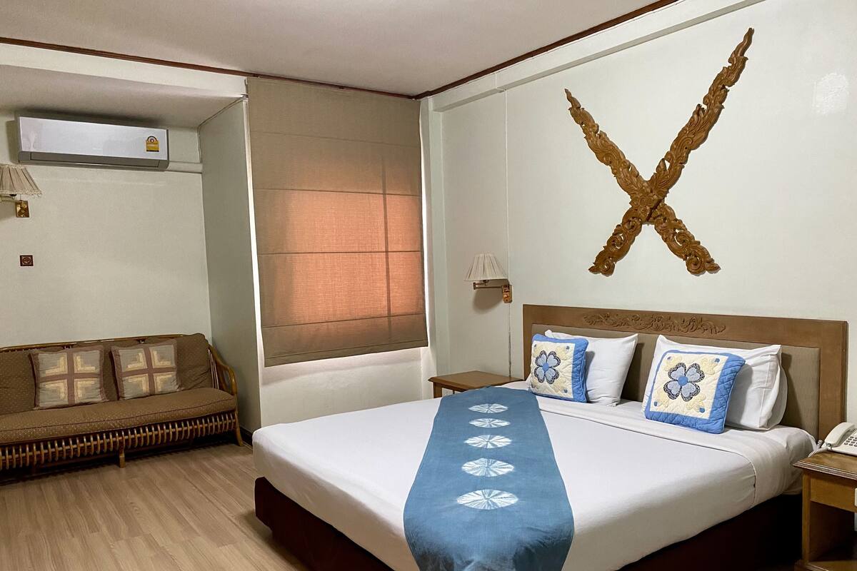 Habitación de hotel con una cama grande, un sofá, aire acondicionado de pared y un elemento decorativo en la pared.