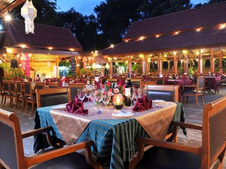 Un espace extérieur aménagé pour les repas, avec des tables pour deux personnes, entourées de chaises en bois.