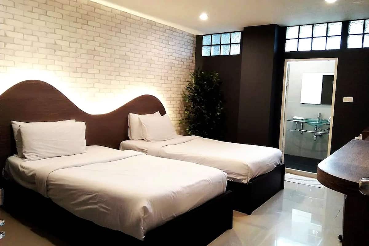 Une chambre d’hôtel avec deux lits, une salle de bain dotée d’une douche en verre et une petite table en bois.