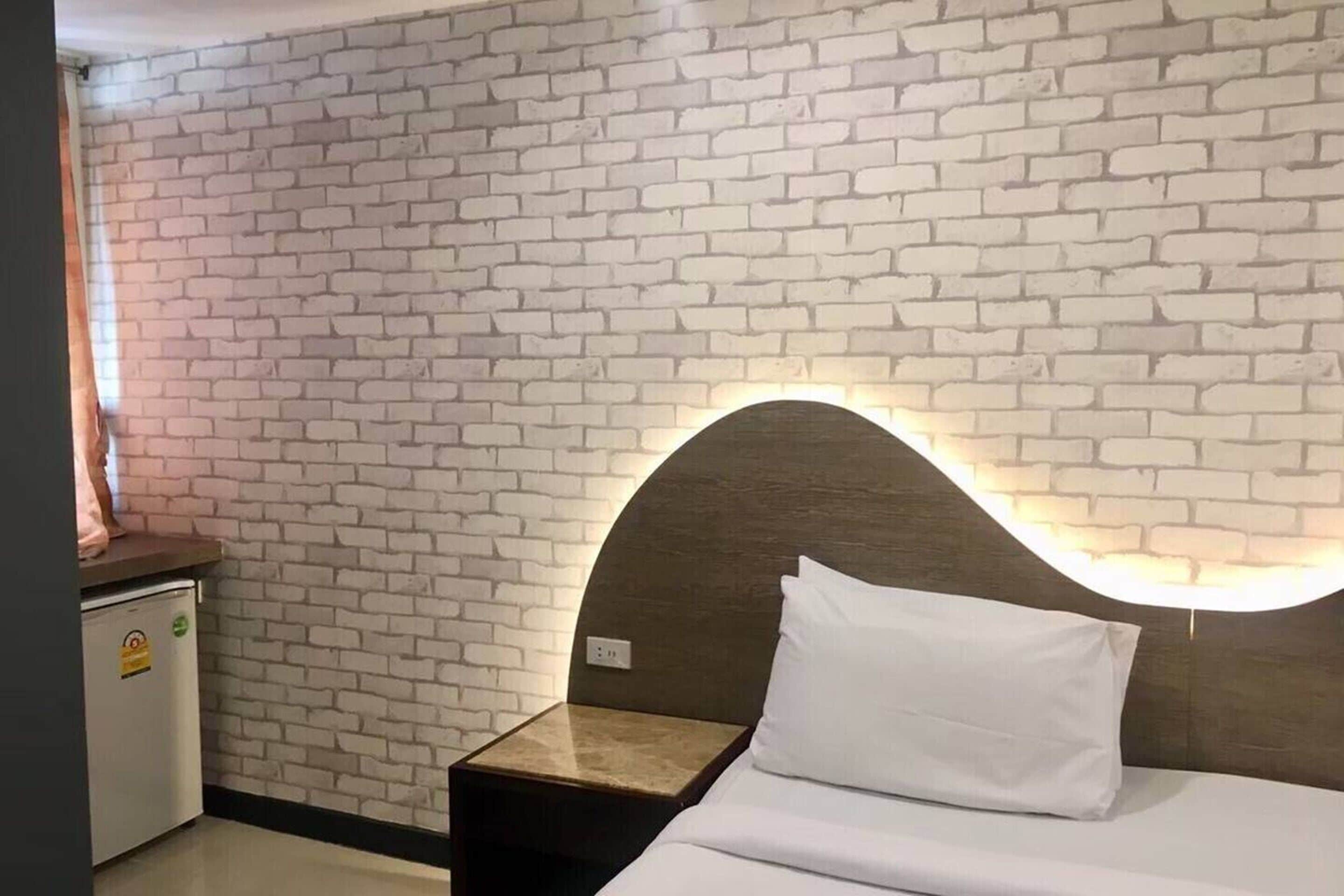 Una habitación de hotel con pared de ladrillo, cabecero de madera, cama con ropa blanca y mesita de noche con lámpara.