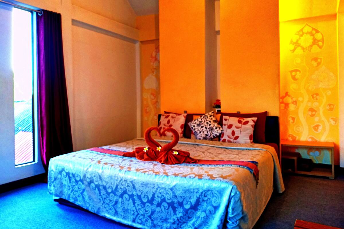 A bedroom with a bed, pillows, a bedside table, and a window with curtains.