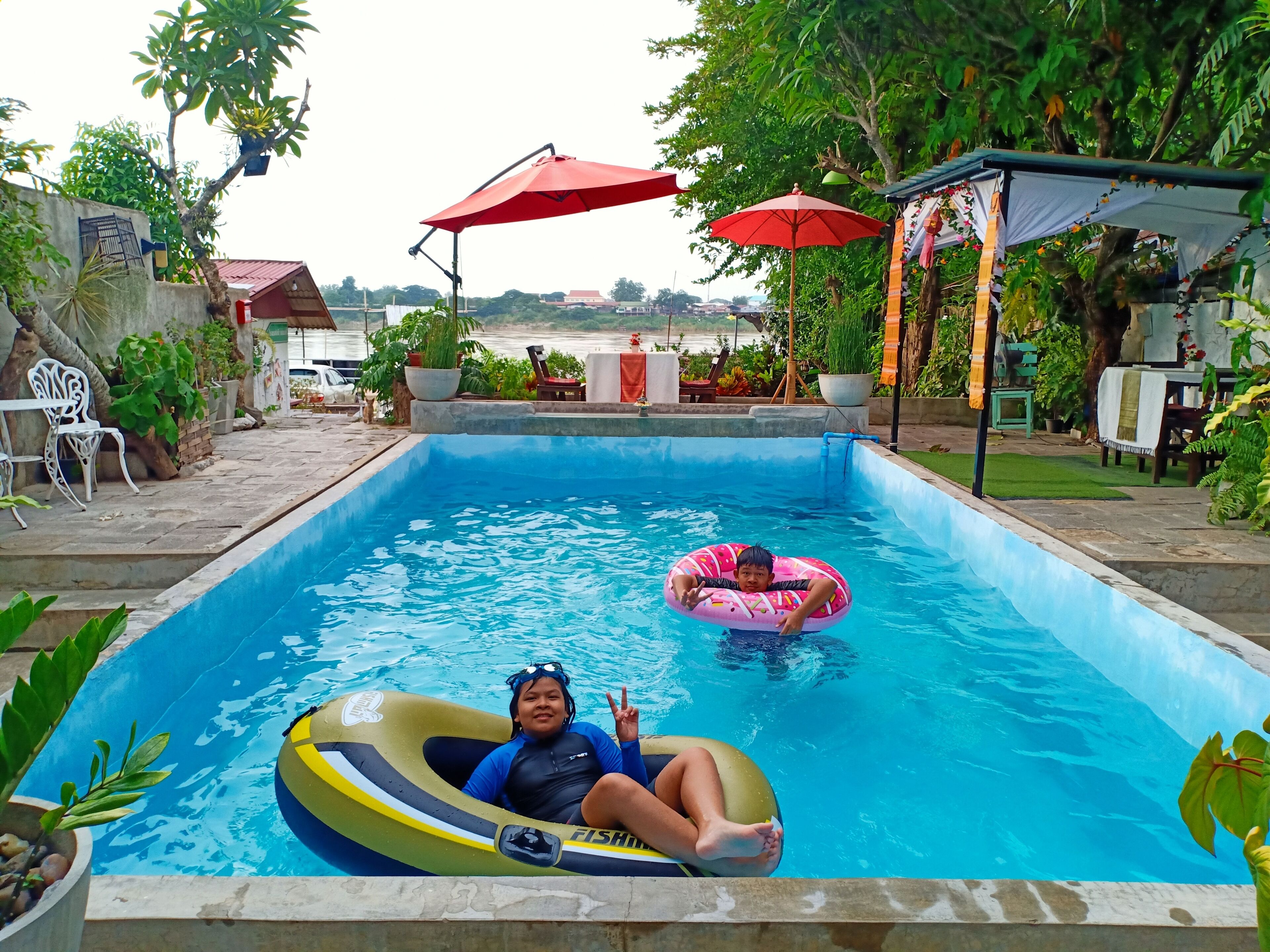 Una piscina con dos flotadores, rodeada de plantas en macetas y mobiliario de exterior.