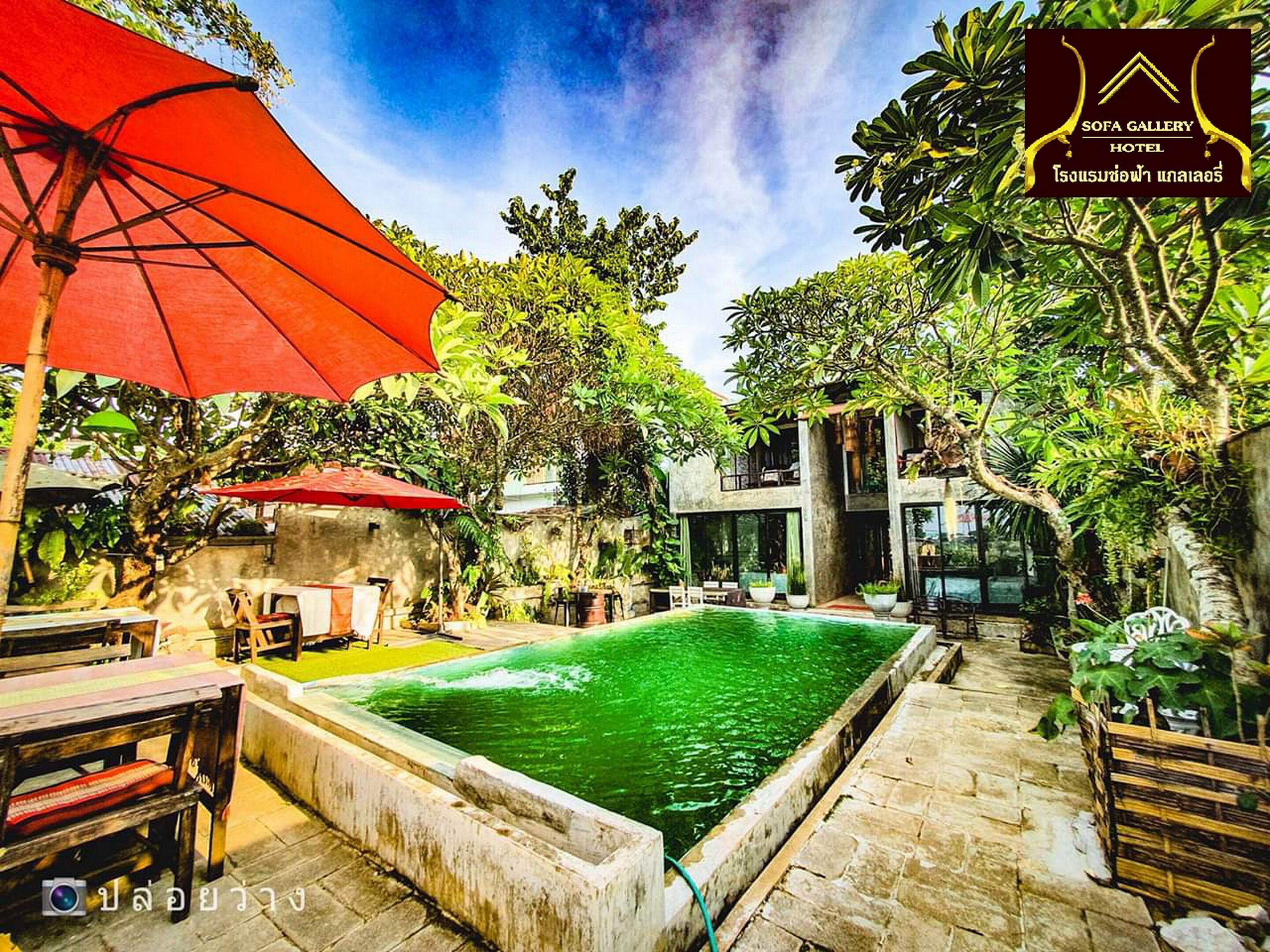 A pool area with a red umbrella, outdoor seating, and lush greenery.