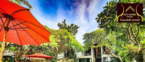 A pool area with a red umbrella, outdoor seating, and lush greenery.