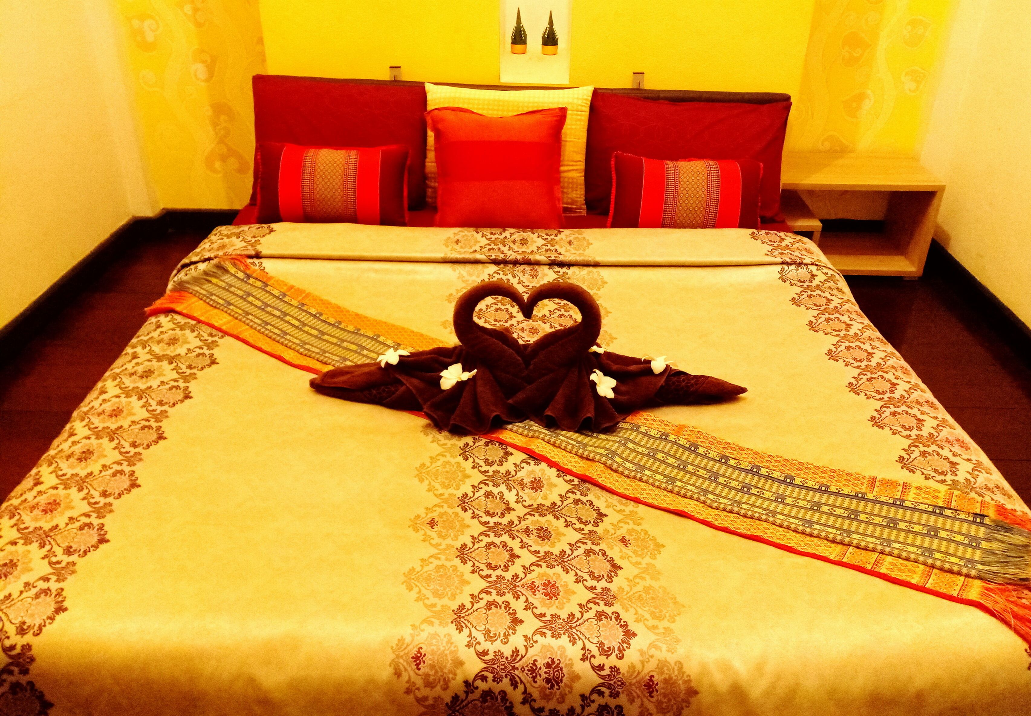 A neatly made bed with a heart-shaped towel and a decorative pillow.
