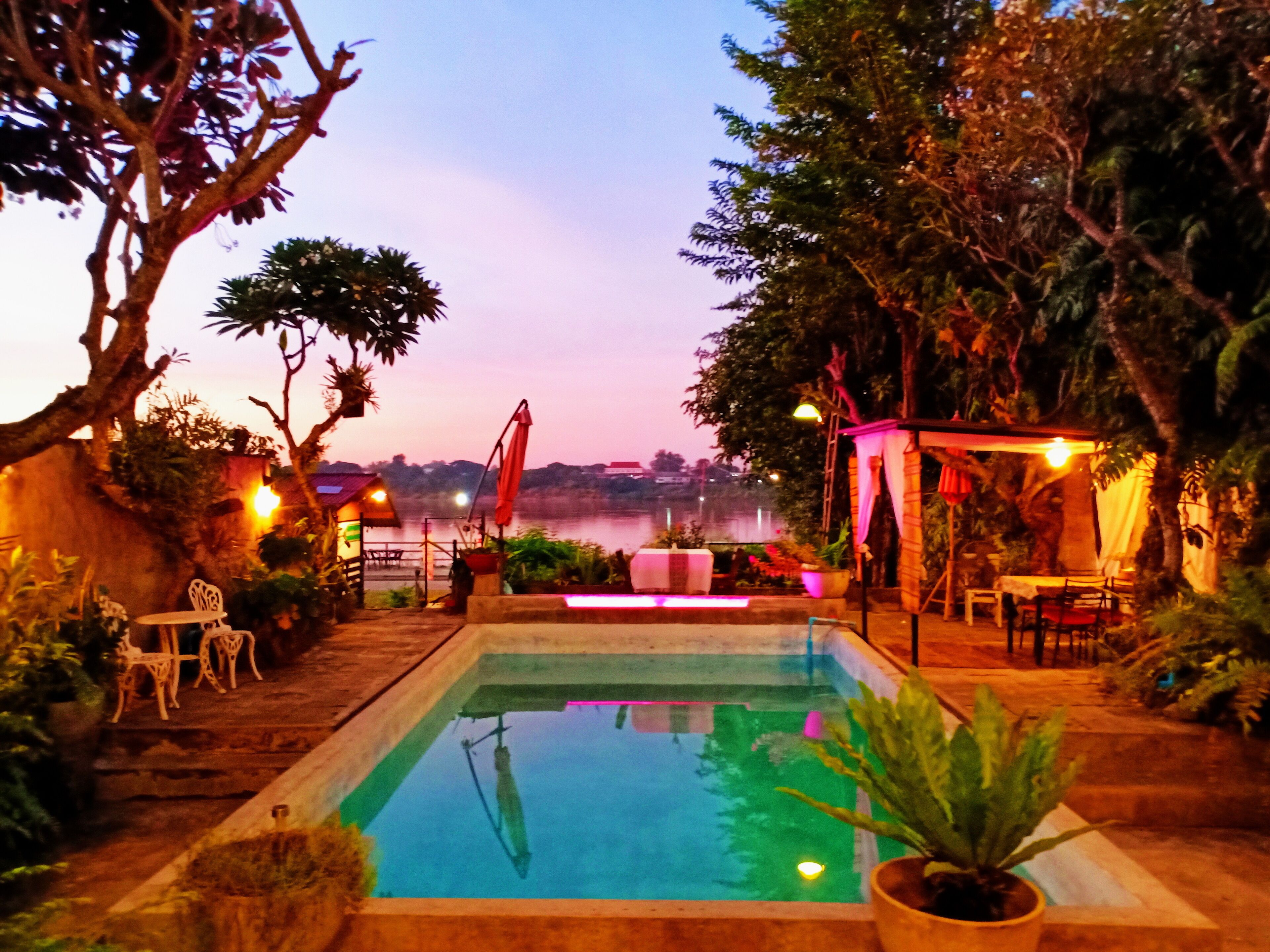 A swimming pool with a view of a body of water, surrounded by trees and outdoor seating.