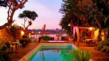 A swimming pool with a view of a body of water, surrounded by trees and outdoor seating.