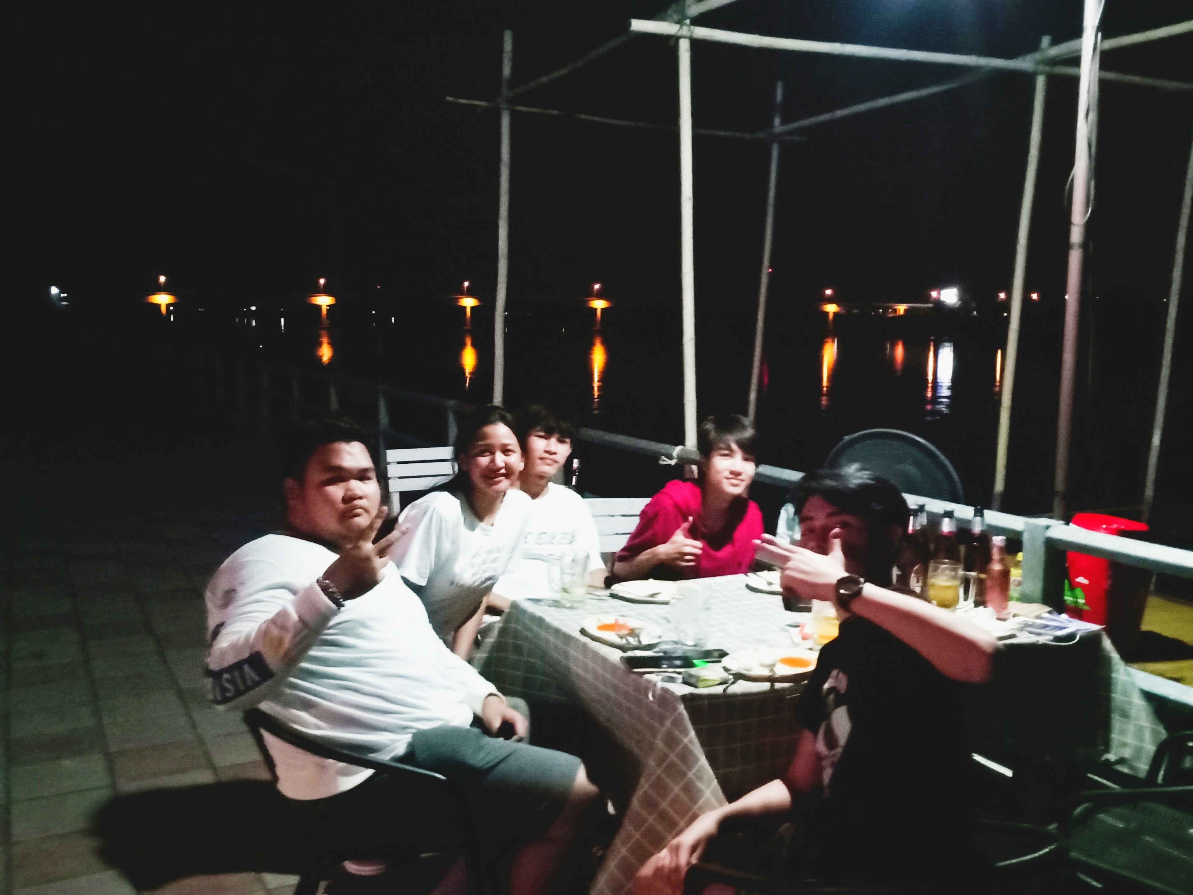 A group of people seated at an outdoor table with a view of the water in the background.