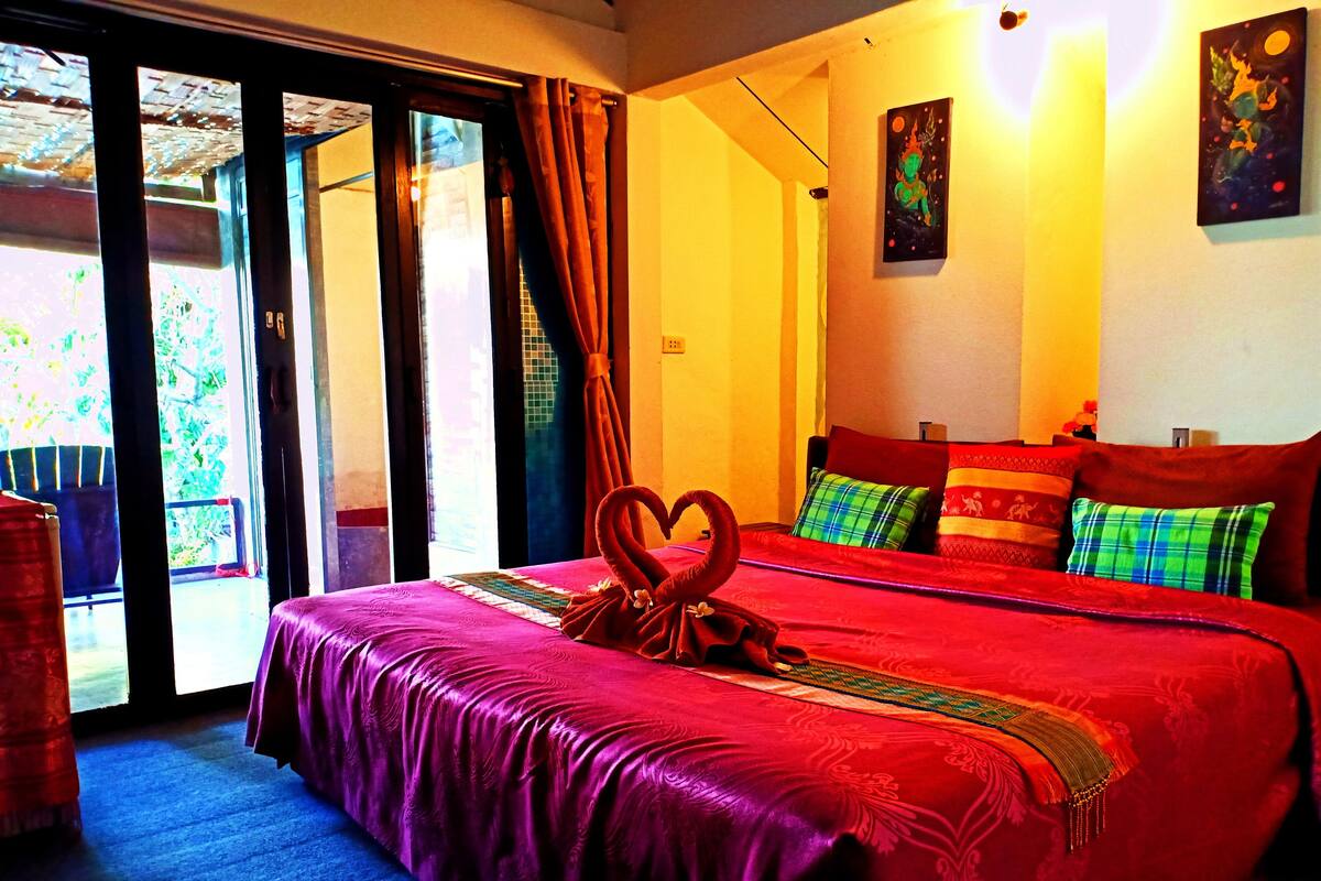 A hotel room with a large bed, a heart-shaped towel, and a painting on the wall.
