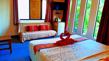 A hotel room with two beds, a desk, a window with curtains, and a view of greenery outside.