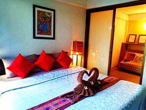 Una habitación de hotel con cama, almohadas rojas, una toalla con forma de corazón, un cuadro en la pared y una mesita de noche con lámpara.