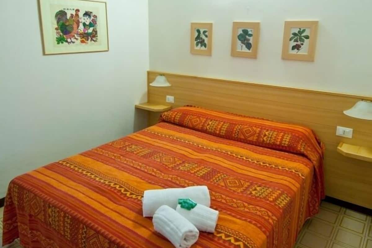 Habitación de hotel con una cama, dos mesitas de noche, una lámpara de pared y un cuadro en la pared.