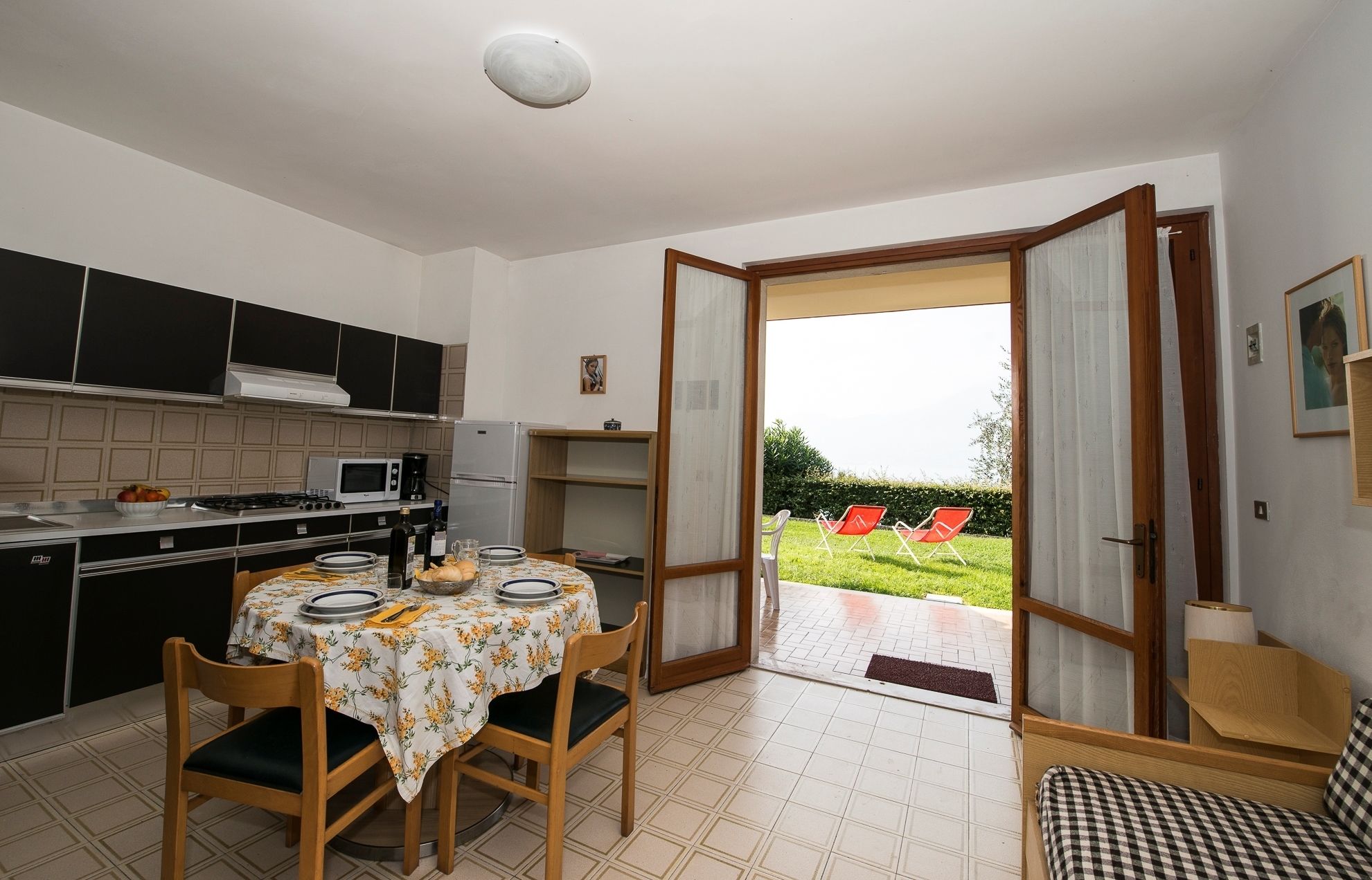 A compact kitchen with modern appliances, a dining area with a table set for two, and a view of a garden through an open door.