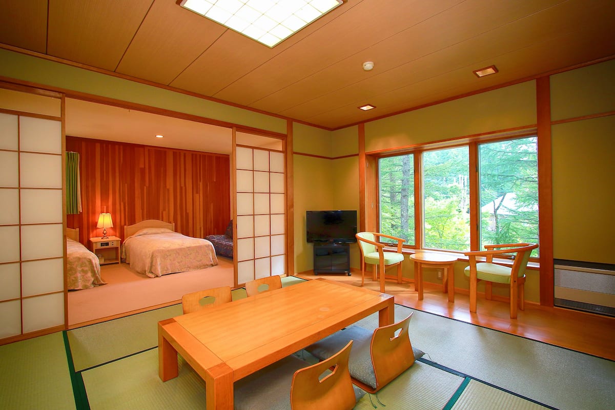 A traditional Japanese-style room with tatami flooring, a wooden dining table, and a TV in the corner.