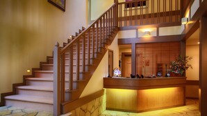 A multi-level interior with a wooden staircase, a reception desk, and a stone-tiled floor. - Hatago SAKURAYA (Yamanakako)