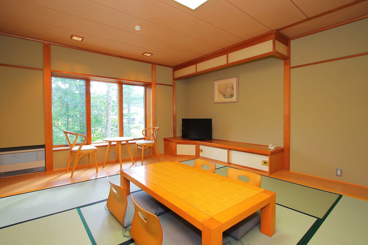 A traditional Japanese-style room with tatami flooring, a wooden table, and chairs.