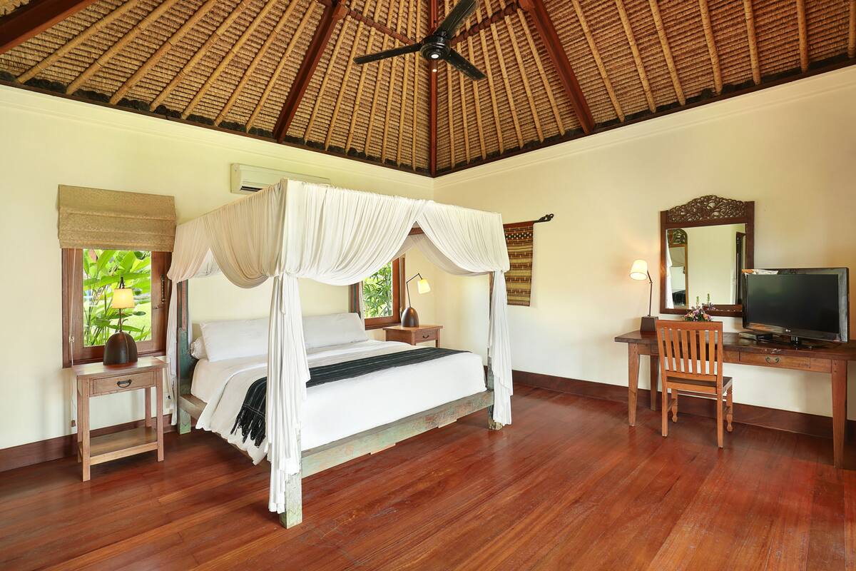 A bedroom with a four-poster bed, wooden desk, chair, and a television.