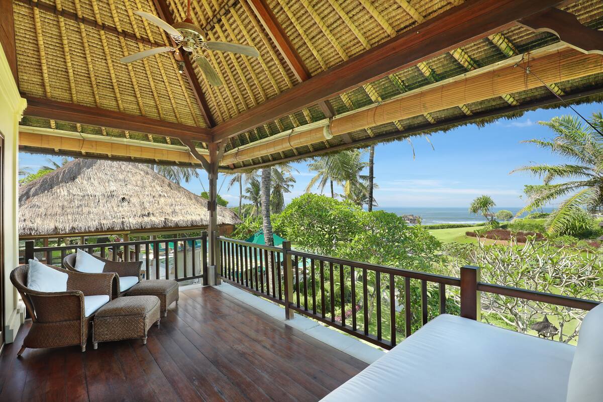 A wooden deck with wicker furniture, a thatched roof, and a view of the ocean.