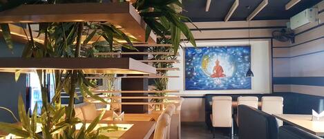 A modern restaurant interior with wooden slatted seating, potted plants, and a large mural on the wall.