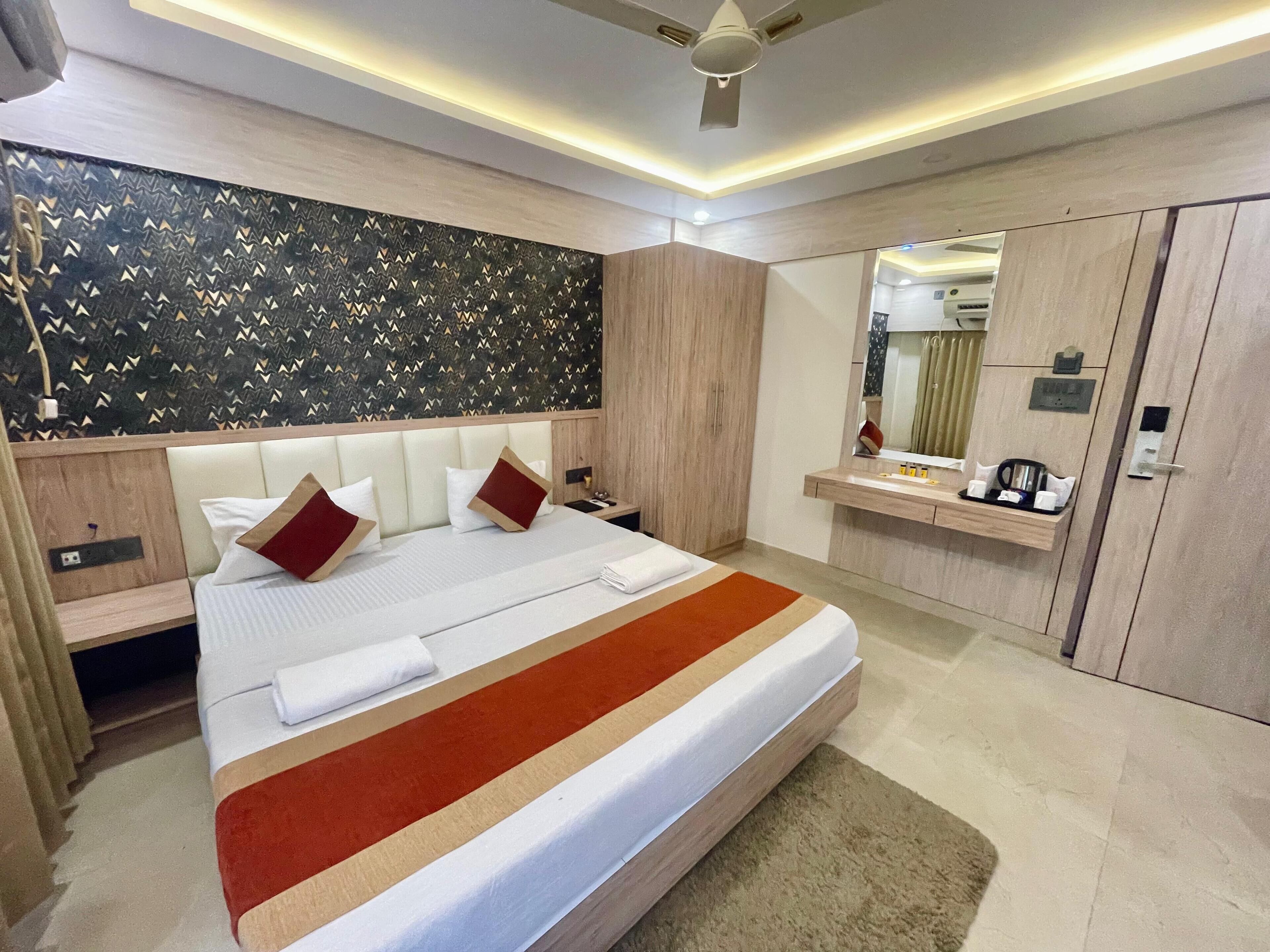 A modern hotel room with a large bed, a wooden headboard, a vanity with a mirror, and a ceiling fan.