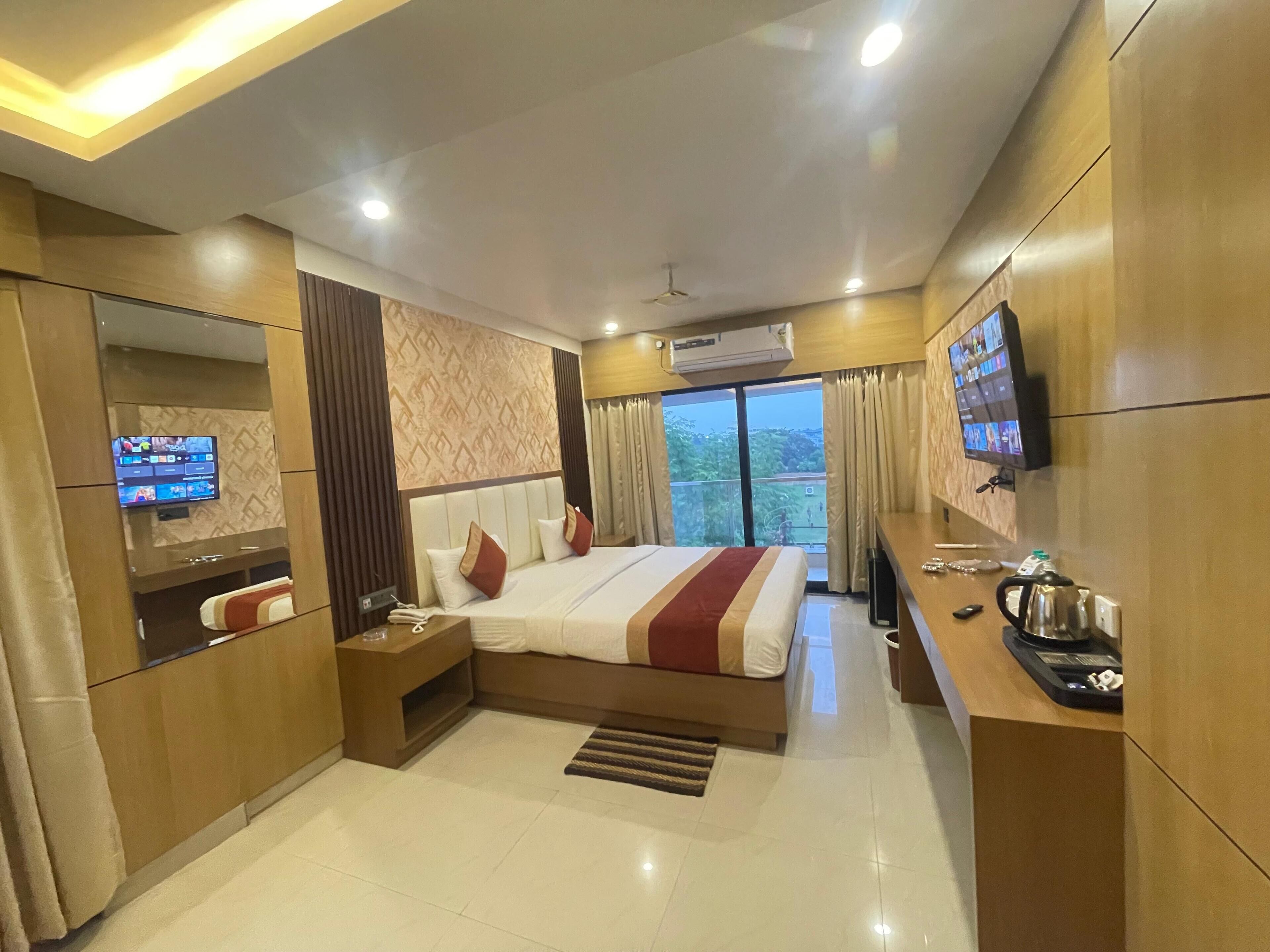 Una habitación de hotel moderna con una cama grande, televisor, aire acondicionado y balcón con cortinas.
