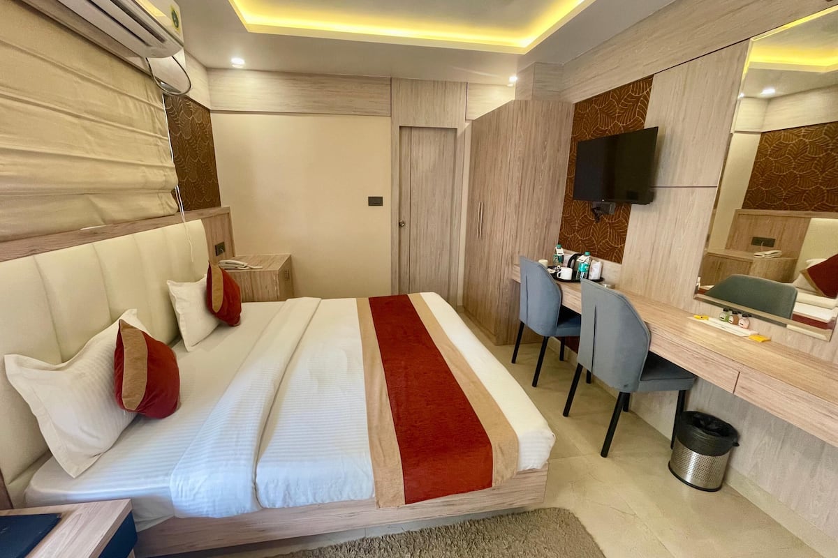 Una habitación de hotel con cama, escritorio, sillas, televisor y espejo.