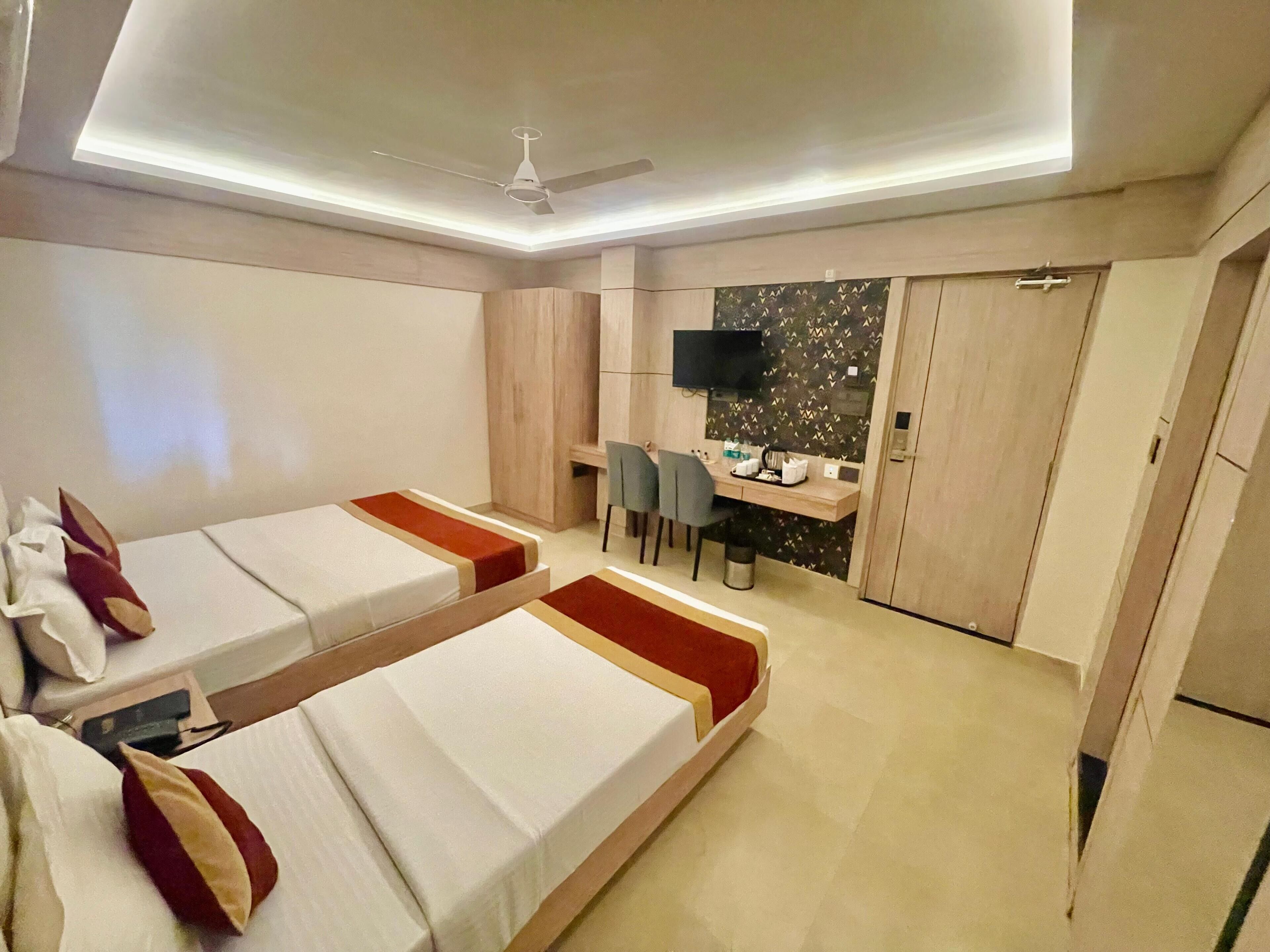 Quarto de hotel com duas camas de solteiro, uma escrivaninha com cadeira, televisão na parede e um guarda-roupa.