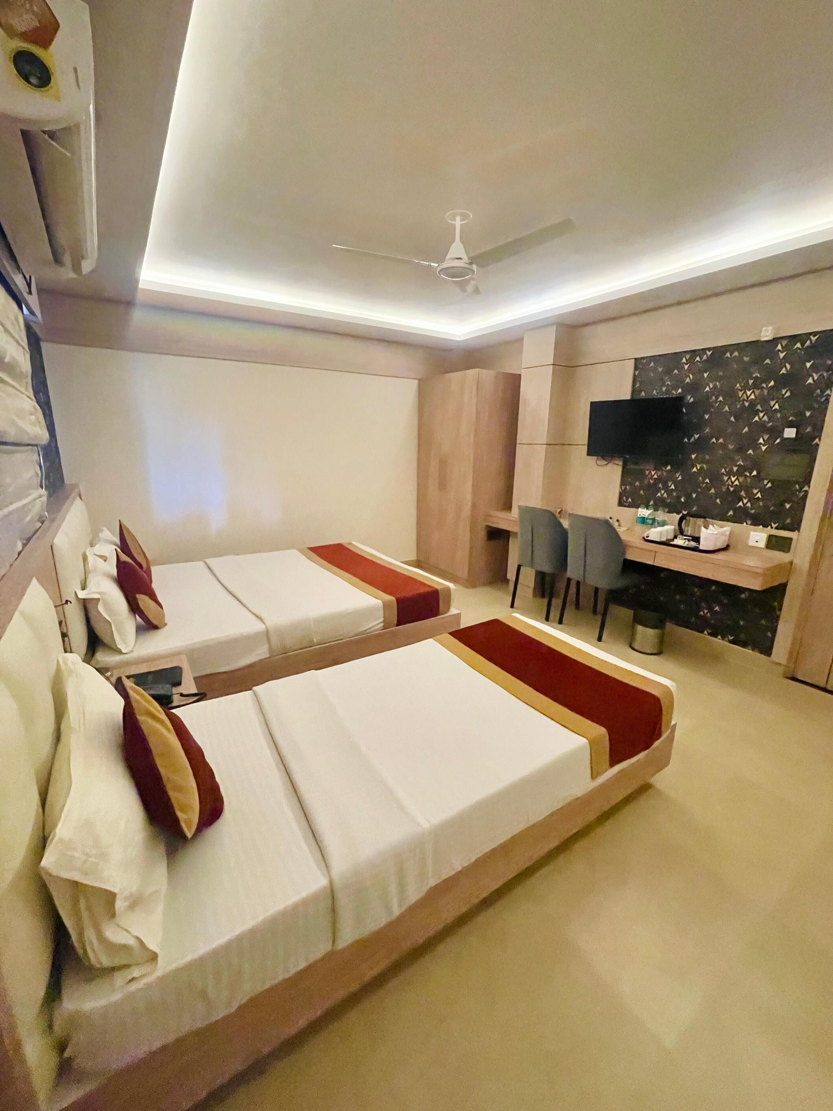 Habitación de hotel con dos camas, un escritorio, una silla, un televisor y un ventilador de techo.