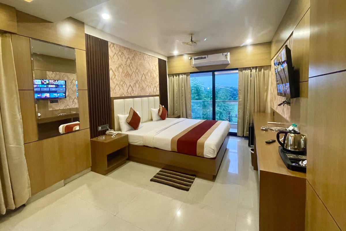 Habitación de hotel moderna con una cama grande, un televisor montado en la pared, un escritorio con un hervidor de agua y vistas a zonas verdes.