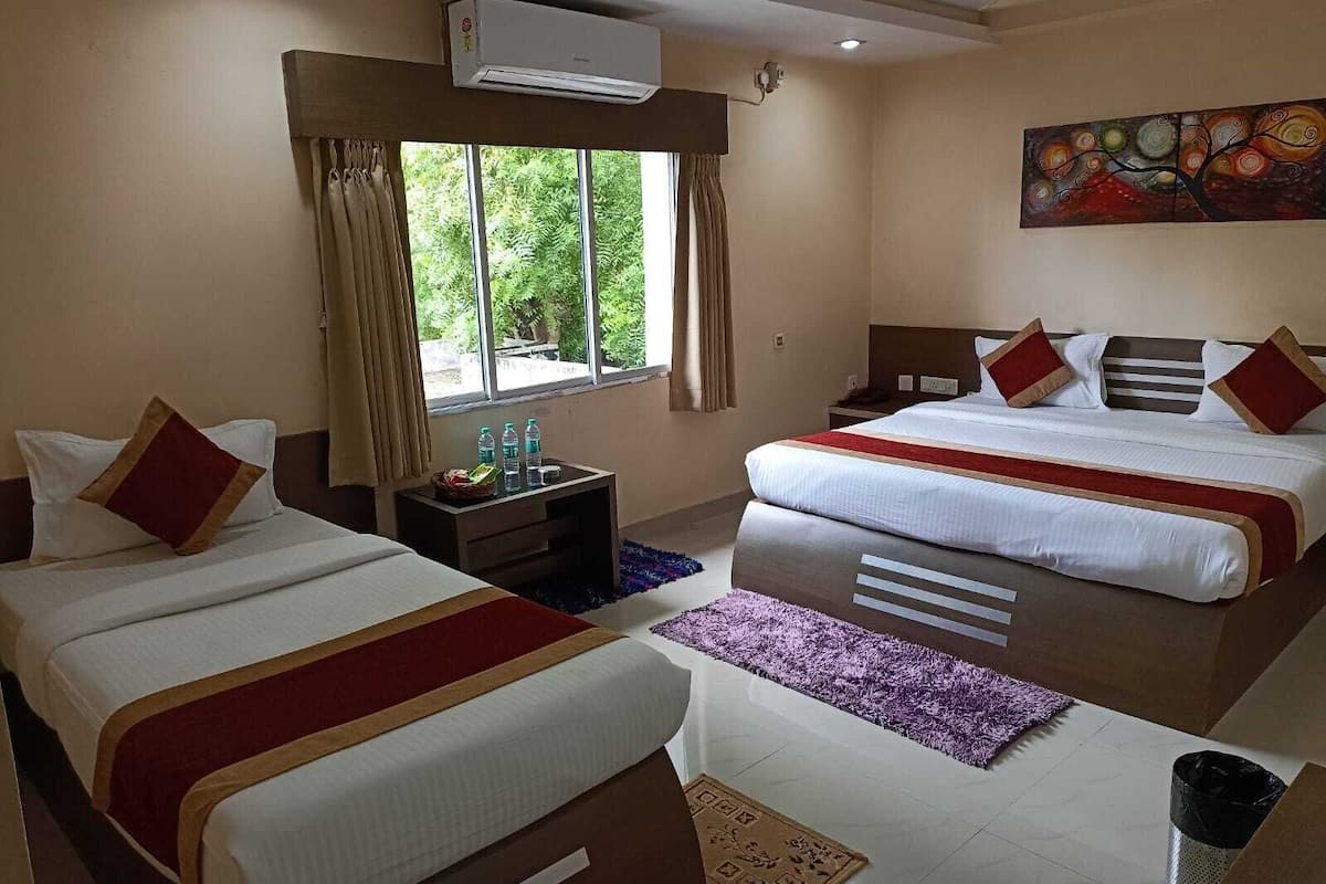 Habitación de hotel con dos camas, una ventana con cortinas, aire acondicionado, una mesita de noche y un cuadro en la pared.