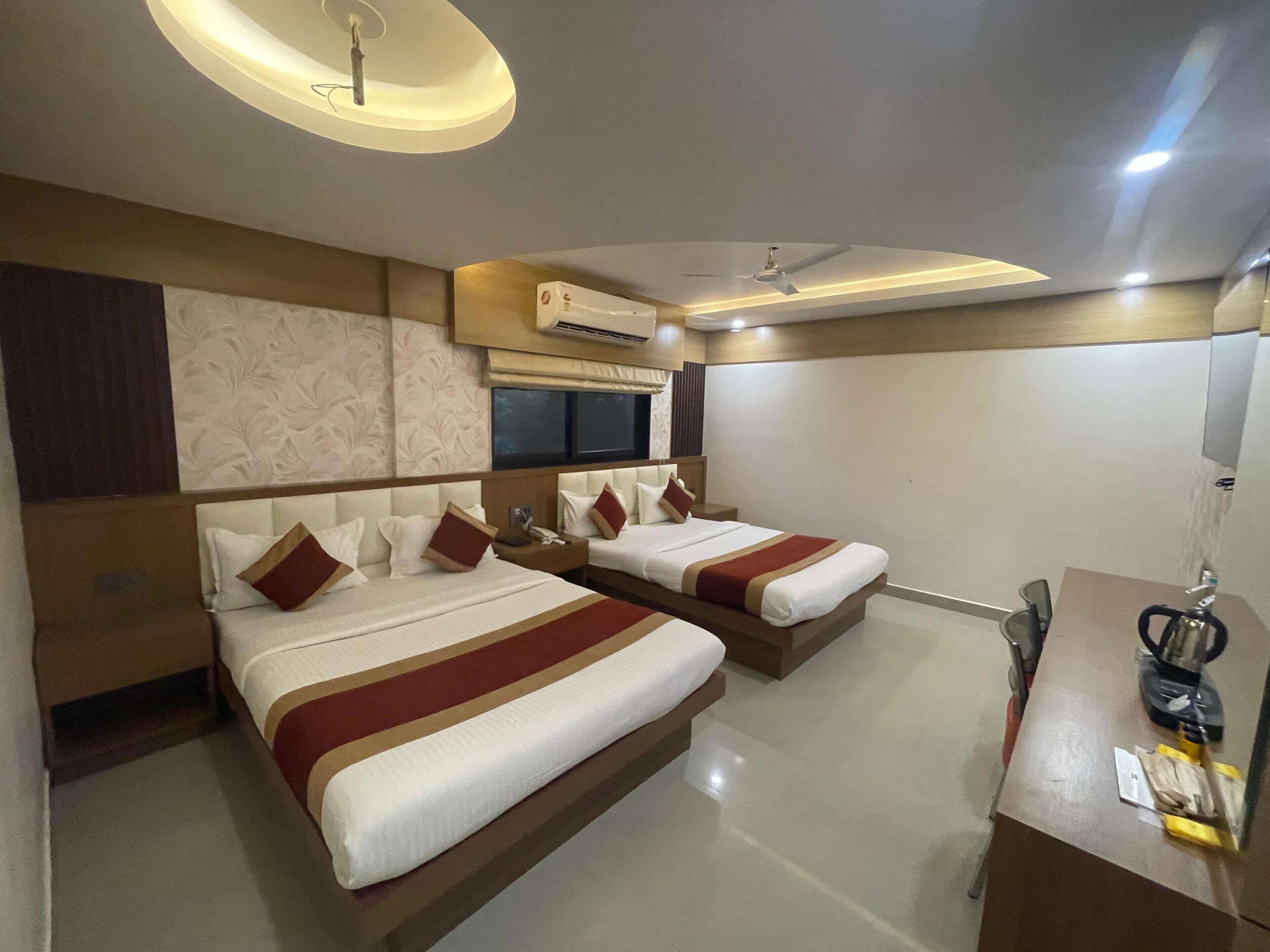 A hotel room with two beds, a desk, a chair, and a ceiling fan.