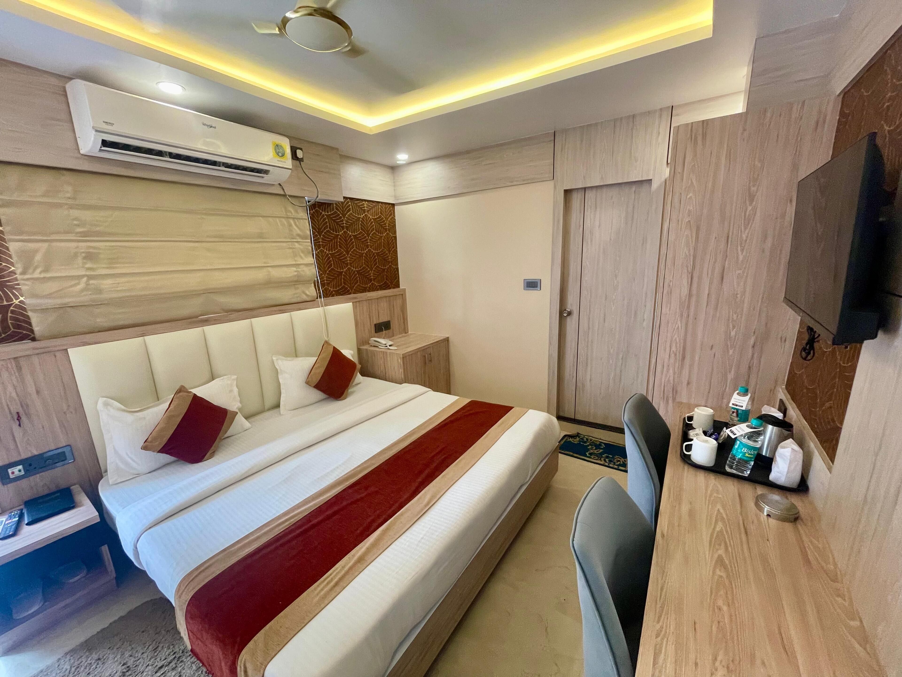 A hotel room with a bed, bedside table, chair, desk, and a TV.