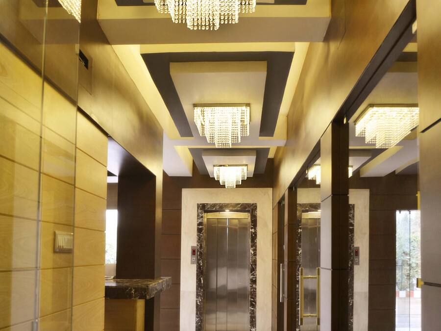 A modern hotel lobby with a marble floor, a central elevator, and a decorative chandelier.