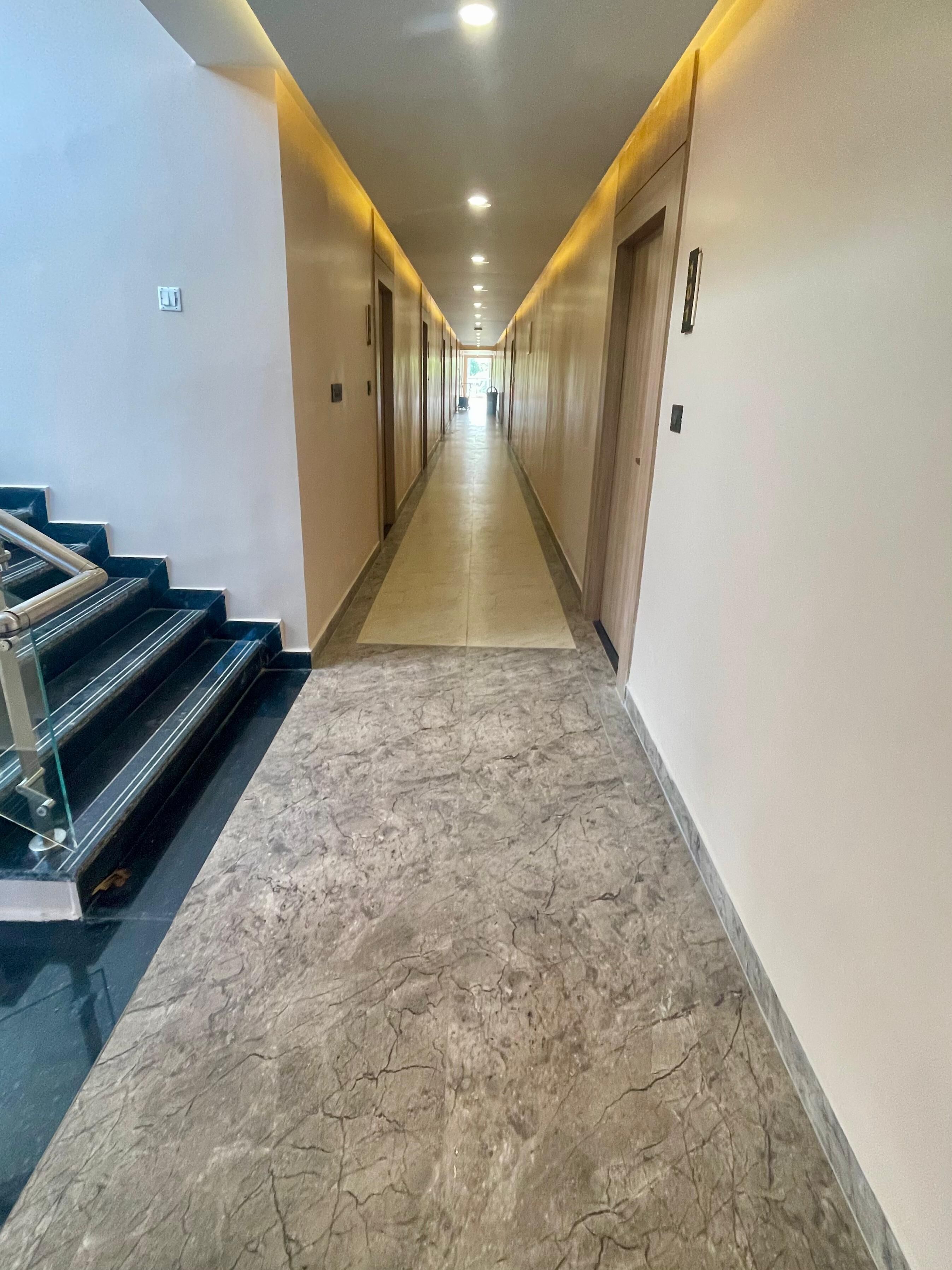 A hotel hallway with marble flooring, a staircase on the left, and doors on both sides leading to rooms.