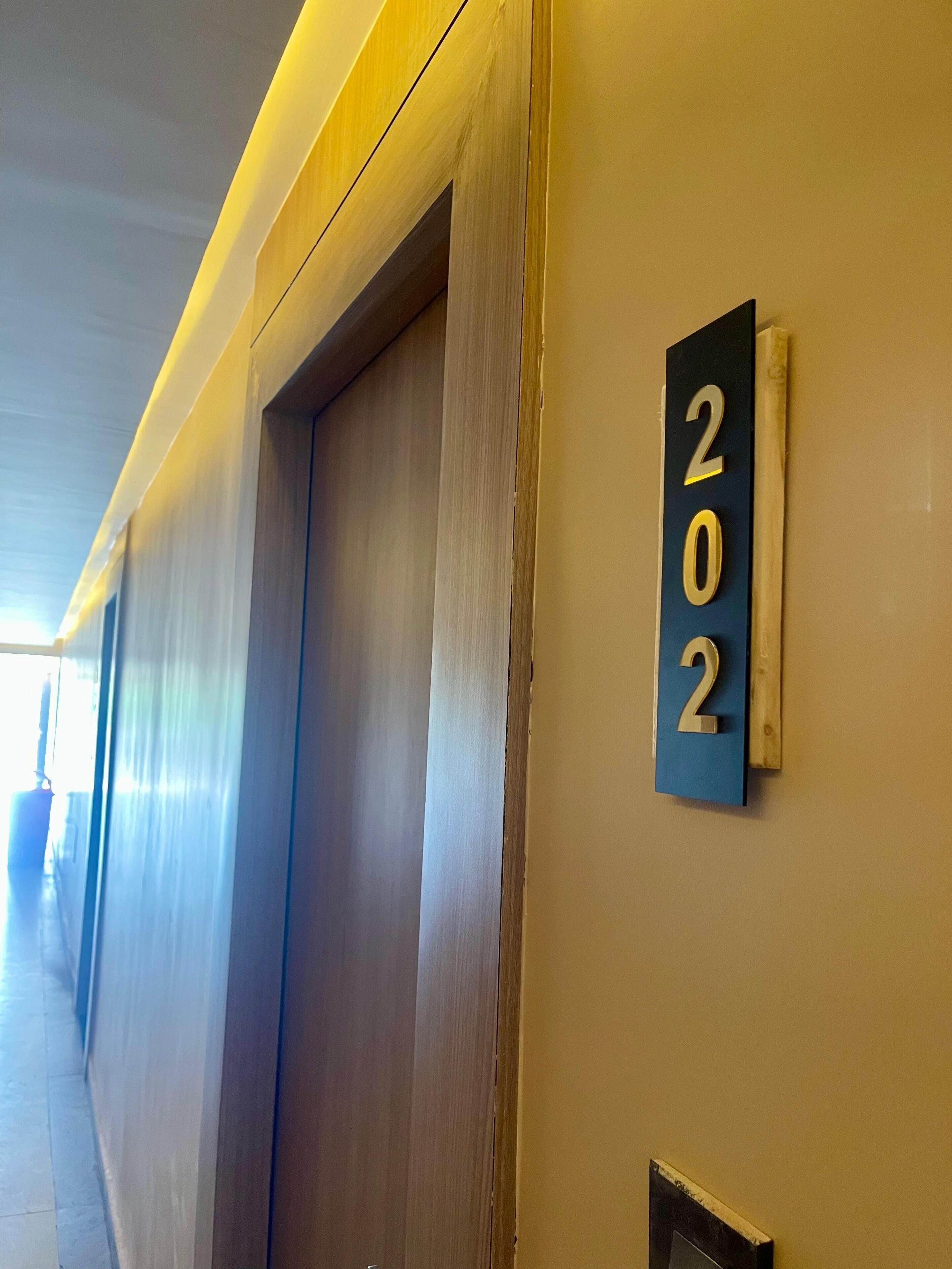 Un couloir avec une porte et une plaque fixée au mur indiquant le numéro de la pièce : 202.