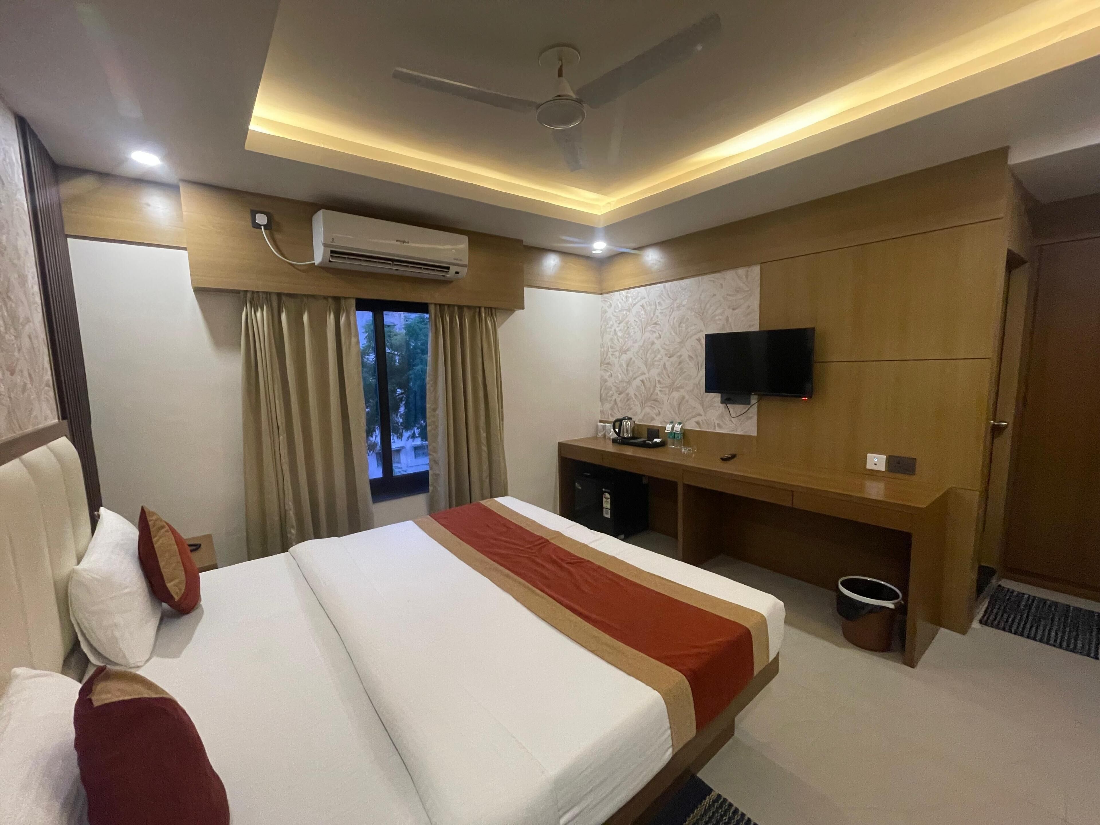 Una habitación de hotel con cama, escritorio, televisor y aire acondicionado.