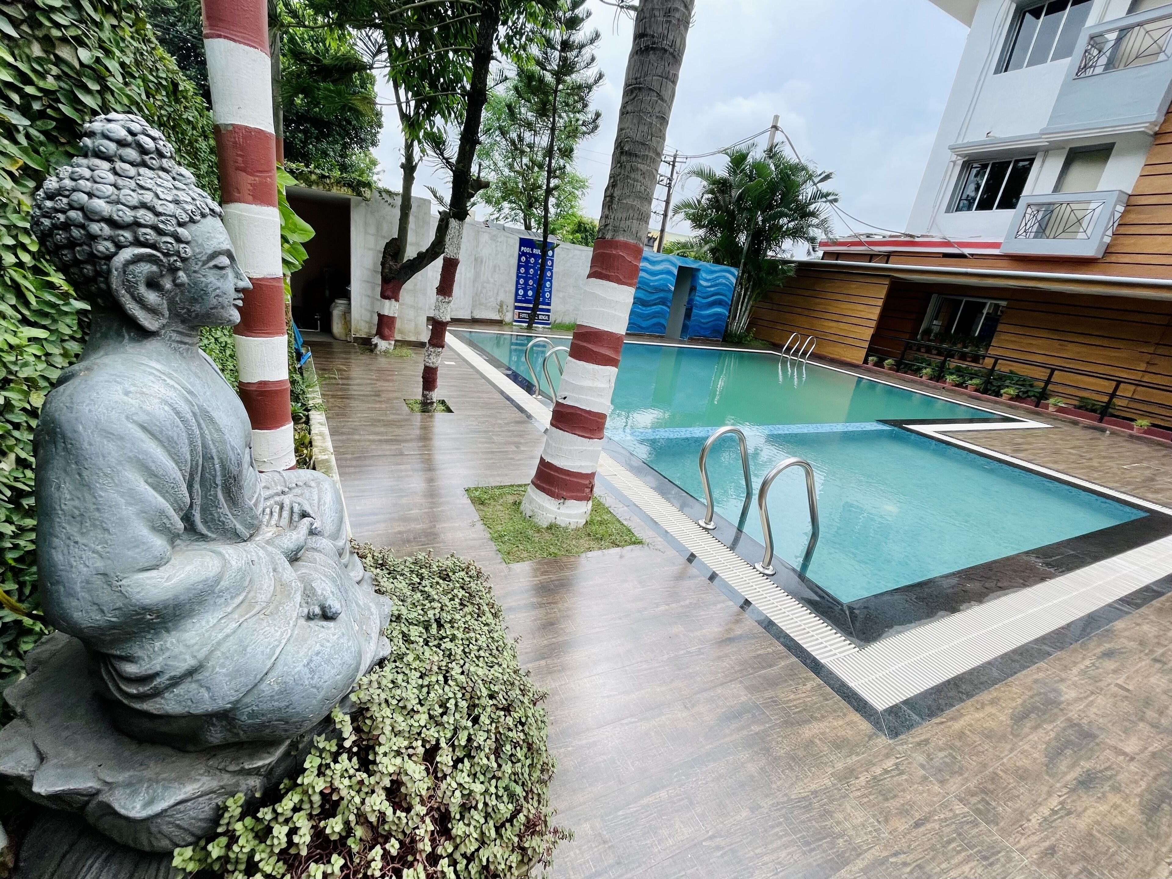 A serene outdoor pool area with a Buddha statue, striped poles, and a modern building in the background.