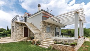 Une maison en pierre dotée d’un balcon, d’une terrasse couverte et d’un escalier en pierre menant à l’entrée.