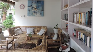 Una habitación con un sofá de bambú, una estantería y un cuadro abstracto grande.
