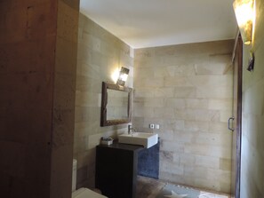 A bathroom with a stone wall, a wooden-framed mirror, a sink, and a shower area.
